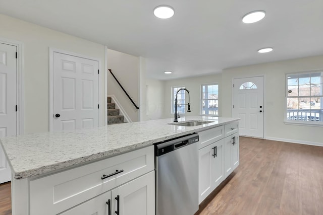 kitchen featuring sink, white cabinetry, stainless steel dishwasher, light stone countertops, and a kitchen island with sink