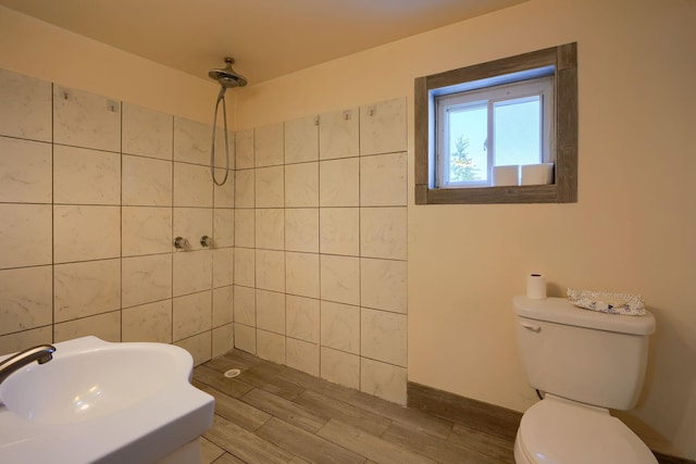 bathroom featuring wood-type flooring, toilet, sink, and a tile shower