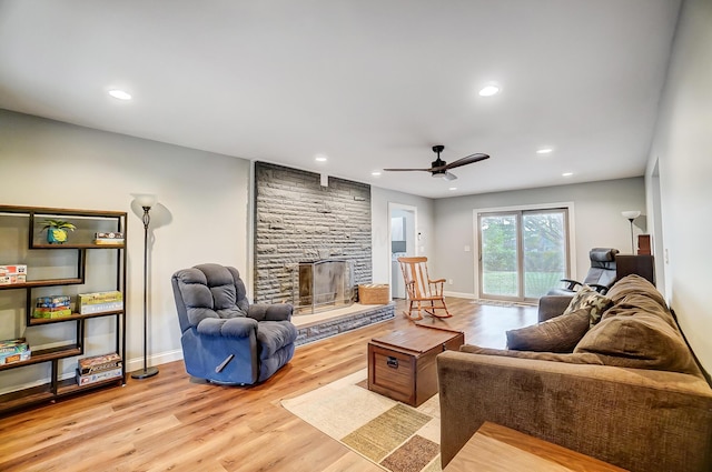 living room featuring ceiling fan, a stone fireplace, and light wood-type flooring