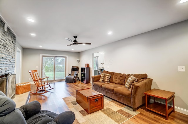 living room with ceiling fan, a stone fireplace, and light hardwood / wood-style floors