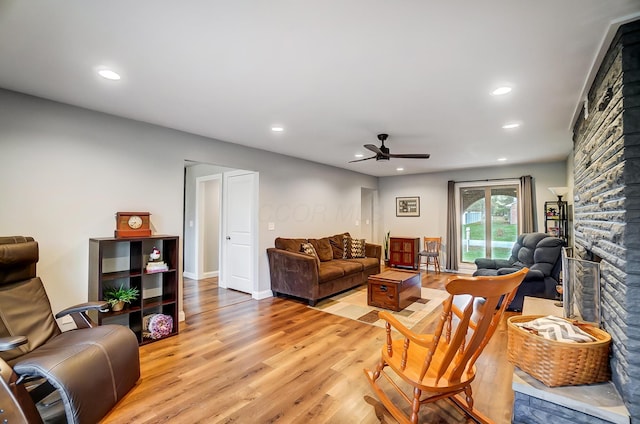 living room with ceiling fan, a stone fireplace, and light wood-type flooring