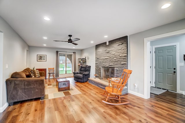 living room with ceiling fan, a stone fireplace, and light hardwood / wood-style floors