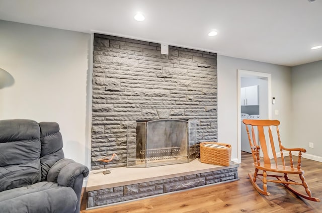 living room featuring hardwood / wood-style flooring, a stone fireplace, and washer and clothes dryer