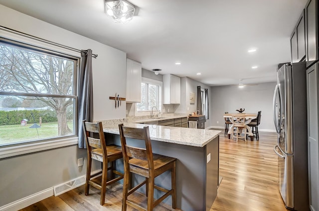 kitchen featuring a breakfast bar, light stone counters, stainless steel fridge, kitchen peninsula, and white cabinets