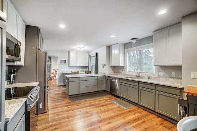 kitchen featuring stainless steel appliances, kitchen peninsula, sink, and light hardwood / wood-style flooring