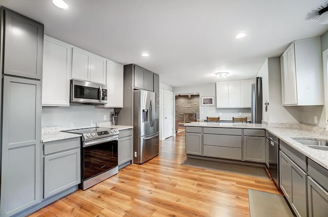 kitchen featuring light stone counters, light wood-type flooring, gray cabinets, kitchen peninsula, and stainless steel appliances