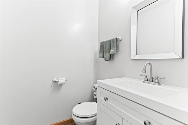 half bathroom with baseboards, toilet, and vanity