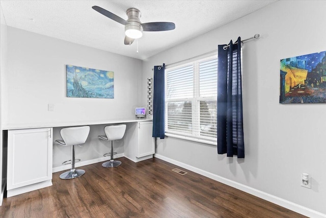 office area featuring visible vents, baseboards, built in desk, wood finished floors, and a ceiling fan