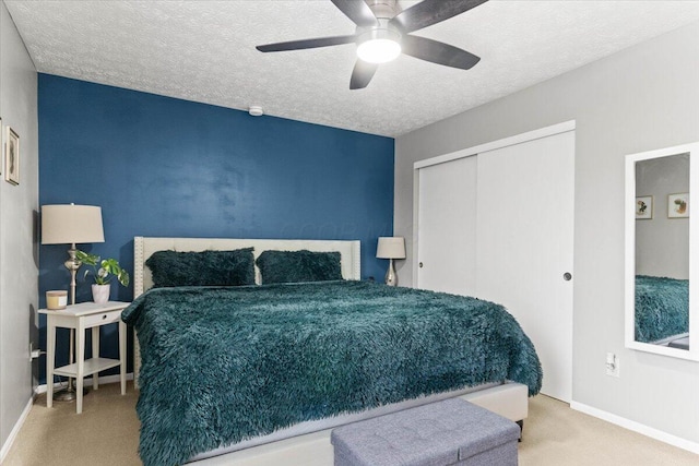 carpeted bedroom with a closet, baseboards, a textured ceiling, and a ceiling fan