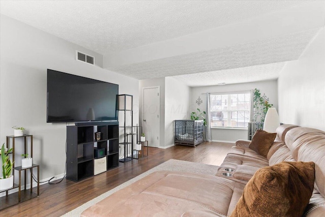 living area with visible vents, baseboards, a textured ceiling, and wood finished floors