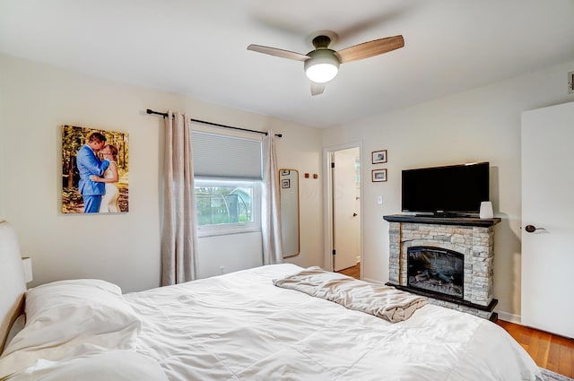 bedroom featuring hardwood / wood-style flooring, a stone fireplace, and ceiling fan