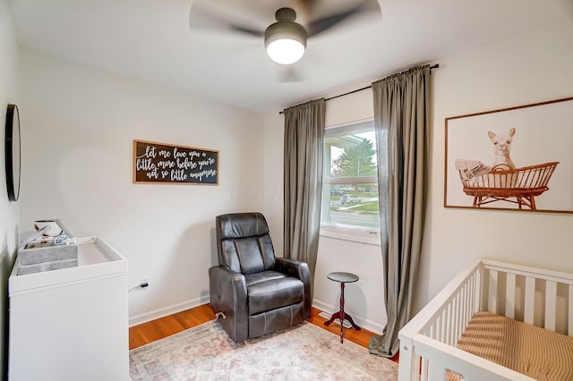 bedroom with hardwood / wood-style floors, a crib, and ceiling fan