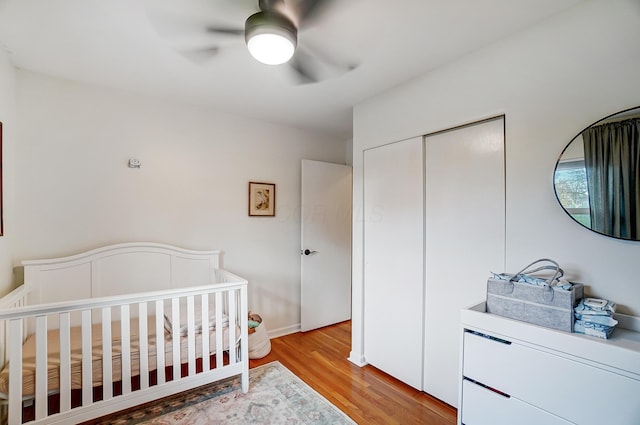 bedroom with a closet, a nursery area, ceiling fan, and light hardwood / wood-style flooring