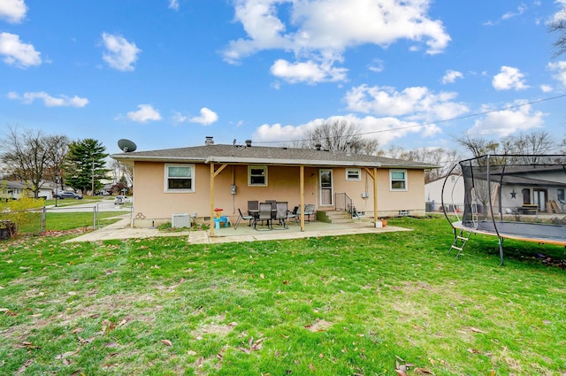 rear view of house with central AC unit, a patio, a trampoline, and a lawn