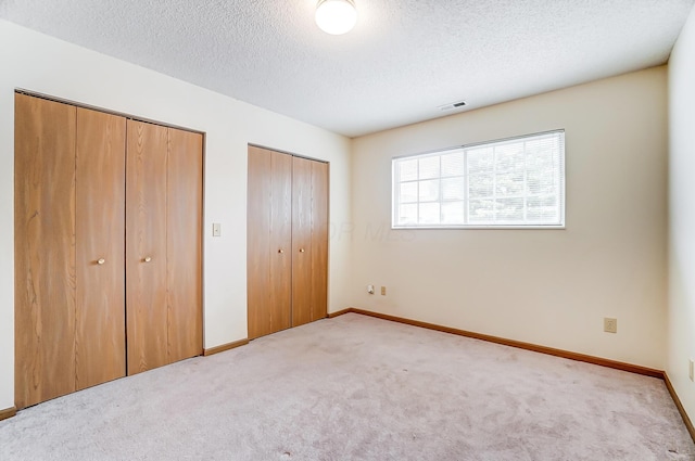 unfurnished bedroom with two closets, light colored carpet, and a textured ceiling