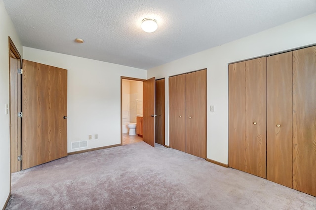 unfurnished bedroom with multiple closets, ensuite bathroom, light carpet, and a textured ceiling