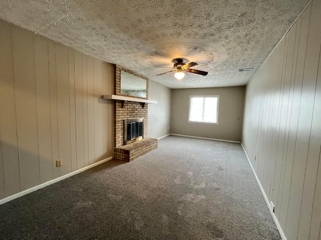 unfurnished living room featuring ceiling fan, wooden walls, carpet floors, a textured ceiling, and a brick fireplace