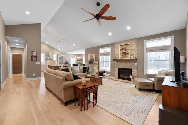 living room with plenty of natural light, a stone fireplace, high vaulted ceiling, and light wood-type flooring