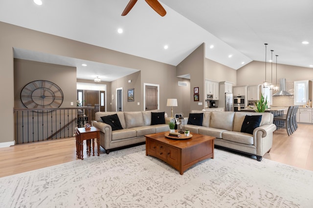 living room with a healthy amount of sunlight, ceiling fan with notable chandelier, high vaulted ceiling, and light hardwood / wood-style flooring