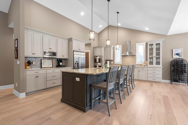 kitchen with wall chimney range hood, a breakfast bar, appliances with stainless steel finishes, a center island with sink, and decorative light fixtures