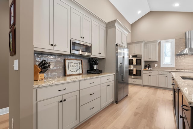 kitchen with wall chimney exhaust hood, white cabinetry, light stone counters, light hardwood / wood-style flooring, and stainless steel appliances