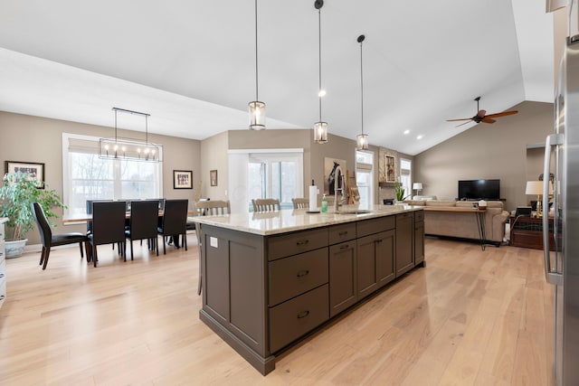 kitchen featuring sink, a center island with sink, light hardwood / wood-style flooring, pendant lighting, and light stone countertops