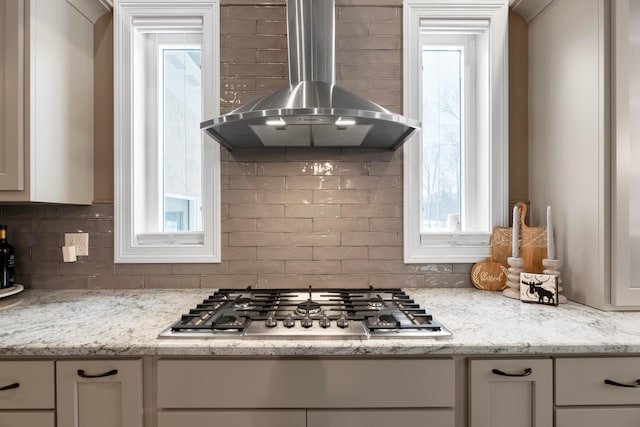 kitchen featuring white cabinetry, stainless steel gas stovetop, light stone counters, and wall chimney range hood