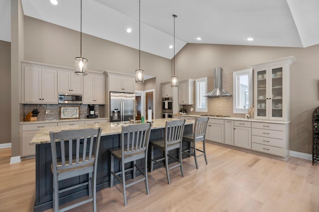 kitchen featuring a large island, wall chimney range hood, pendant lighting, white cabinetry, and stainless steel appliances