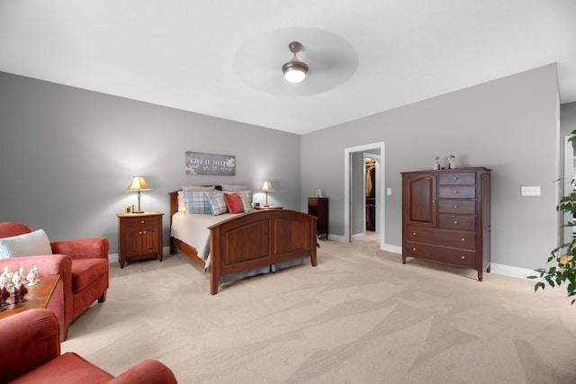 bedroom featuring a walk in closet, light colored carpet, ceiling fan, and a closet