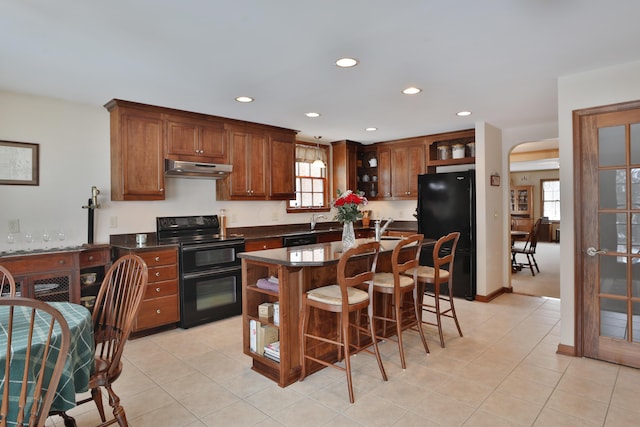 kitchen with light tile patterned floors, black appliances, sink, and a kitchen bar