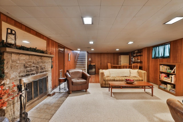 living room featuring a stone fireplace and wood walls