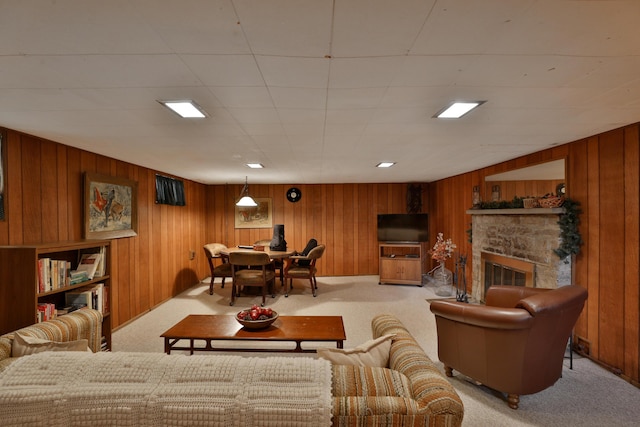 carpeted living room with wooden walls and a stone fireplace