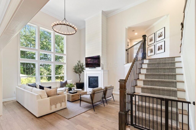 living room with crown molding, light hardwood / wood-style flooring, a chandelier, and a towering ceiling