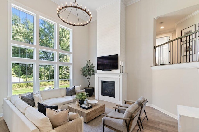 living room featuring crown molding, an inviting chandelier, light wood-type flooring, a fireplace, and a high ceiling