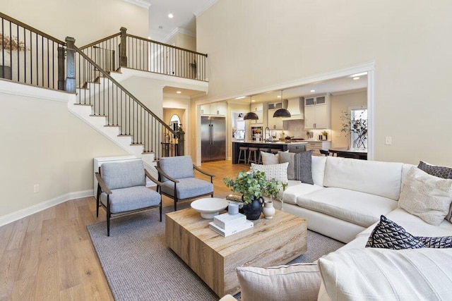 living room featuring a towering ceiling, light hardwood / wood-style flooring, and ornamental molding