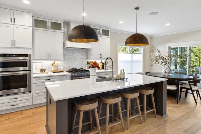 kitchen featuring white cabinets, hanging light fixtures, a kitchen island with sink, stainless steel appliances, and crown molding