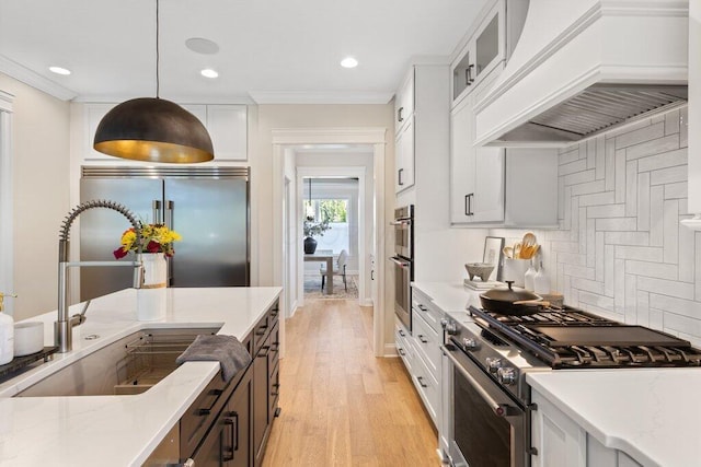 kitchen featuring sink, white cabinetry, high quality appliances, custom range hood, and pendant lighting