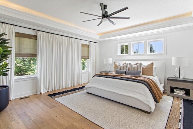 bedroom with multiple windows, crown molding, light hardwood / wood-style floors, and a raised ceiling