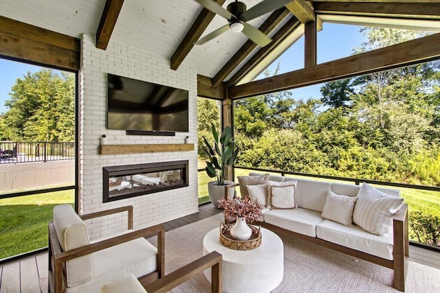 sunroom with ceiling fan, lofted ceiling with beams, and a brick fireplace