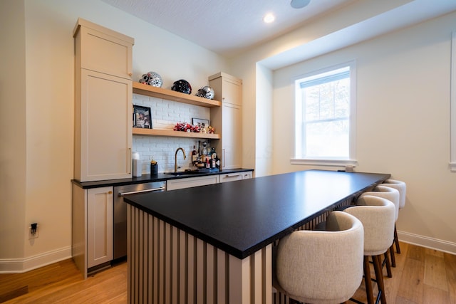 bar featuring tasteful backsplash, sink, light hardwood / wood-style floors, and dishwasher