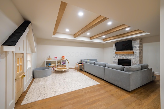 living room with beam ceiling, a stone fireplace, and light hardwood / wood-style flooring