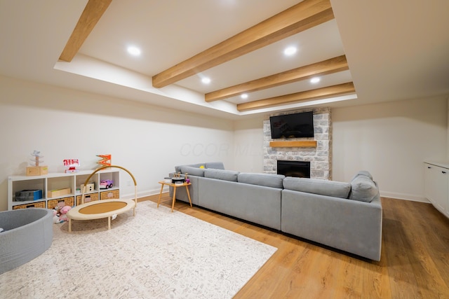 living room featuring beam ceiling, wood-type flooring, and a stone fireplace