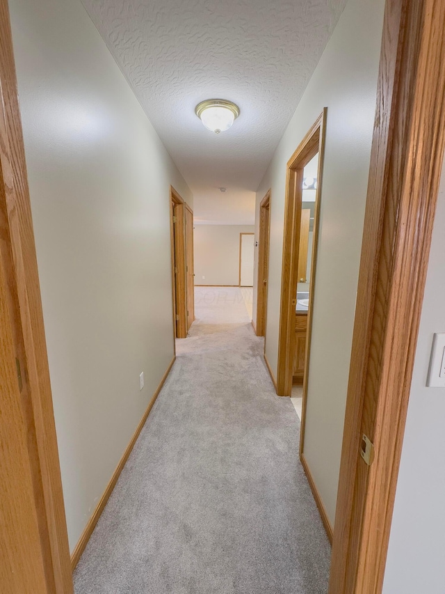 hallway featuring light carpet and a textured ceiling