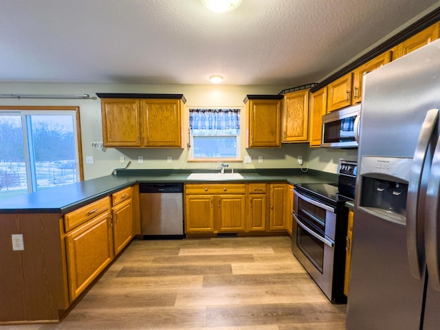 kitchen with sink, light hardwood / wood-style flooring, a textured ceiling, kitchen peninsula, and stainless steel appliances