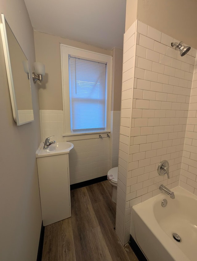 full bathroom with hardwood / wood-style flooring, tile walls, vanity, toilet, and tiled shower / bath