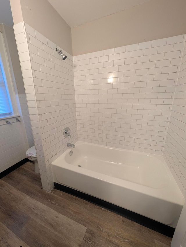 bathroom with tiled shower / bath, wood-type flooring, toilet, and tile walls