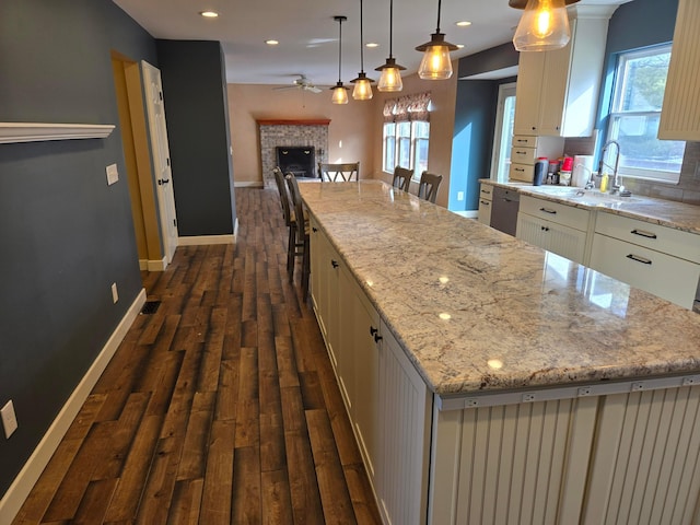 kitchen featuring sink, hanging light fixtures, dark hardwood / wood-style floors, a spacious island, and light stone countertops