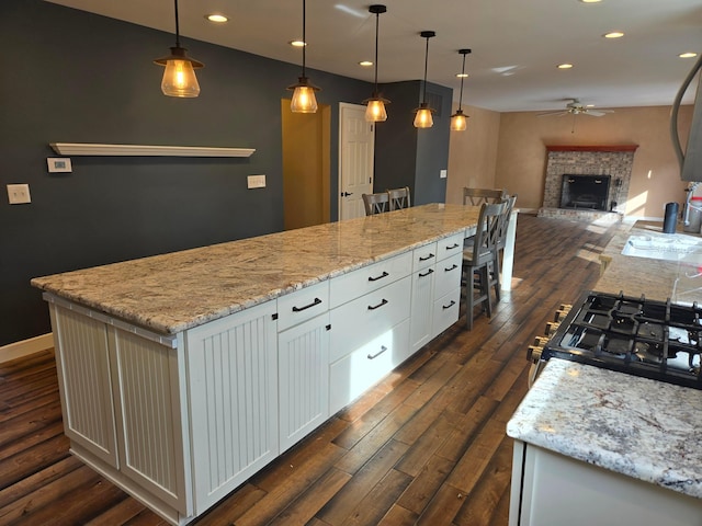 kitchen featuring dark wood-type flooring, ceiling fan, white cabinetry, a spacious island, and decorative light fixtures