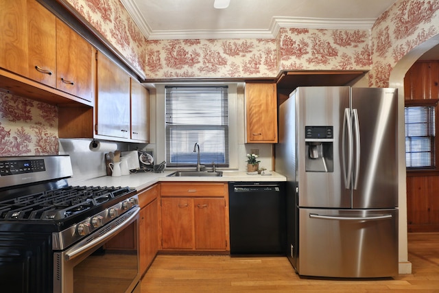 kitchen with stainless steel appliances, ornamental molding, sink, and light hardwood / wood-style floors