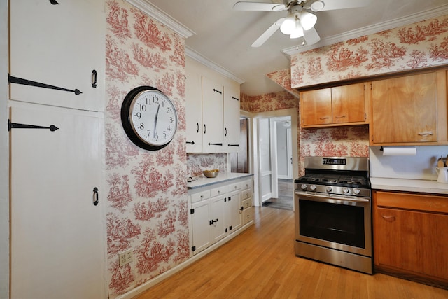 kitchen featuring crown molding, light hardwood / wood-style flooring, ceiling fan, stainless steel gas range oven, and white cabinets